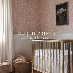 May include: A gold crib with a white mattress and a white ruffle. The crib is in a nursery with a pink floral wallpaper, a white curtain, and two wicker baskets.