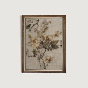 Op de afbeelding: Een ingelijste bloemenprint met een botanische illustratie van gele bloemen en groene bladeren op een beige achtergrond. Het kunstwerk is ingesloten in een bruine houten lijst, wat een vintage esthetiek cre&euml;ert. De print heeft een getextureerd uiterlijk.