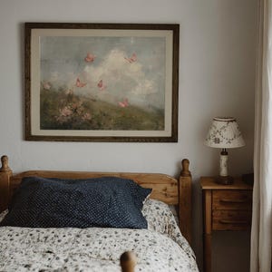 May include: A bedroom scene featuring a wooden bed with a floral patterned quilt and a navy blue pillow with white polka dots. A framed painting of butterflies hangs above the bed. A small wooden nightstand with a lamp is beside the bed.