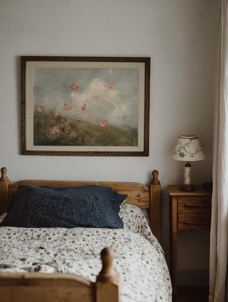 May include: A bedroom scene featuring a wooden bed with a floral patterned quilt and a navy blue pillow with white polka dots. A framed painting of butterflies hangs above the bed. A small wooden nightstand with a lamp is beside the bed.