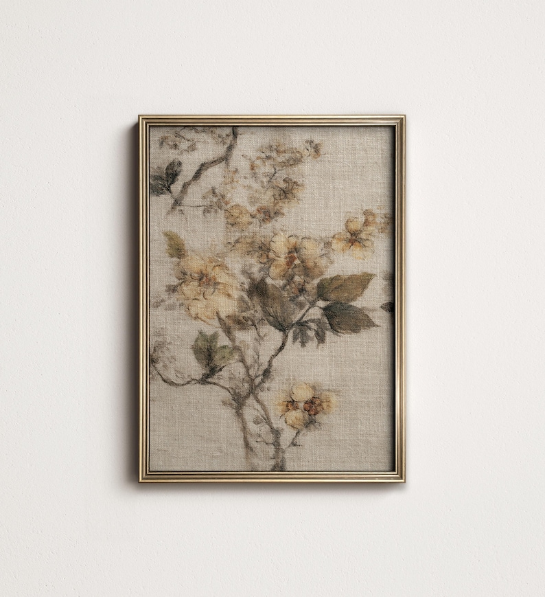Op de afbeelding: Een ingelijste bloemenprint met een botanische illustratie van gele en bruine bloemen en bladeren. Het kunstwerk is geplaatst tegen een neutrale achtergrond en omlijst in een goudkleurige lijst. De print heeft een vintage esthetiek.