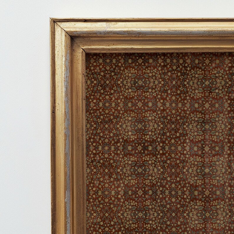 May include: Close-up of a framed artwork. The gold frame has a distressed finish. The artwork displays a detailed, repeating pattern in red, brown, and beige, suggesting a vintage or antique style. The artwork is likely a textile or fabric.