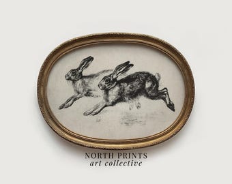 May include: An oval framed print featuring two running hares in a vintage style. The artwork is in black and white, with the hares depicted in mid-leap. The frame is gold-toned, and the print has the text "NORTH PRINTS art collective" at the bottom.