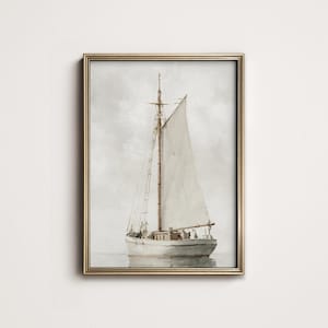 May include: A framed watercolor painting of a sailboat on calm water. The boat is white with a beige sail and a brown mast. The frame is gold. The background is a soft, muted gray.