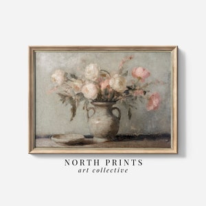 May include: A framed vintage-style painting featuring a bouquet of white and pink flowers in a vase. The vase is a muted gray color, and a small dish sits to the left. The artwork is signed "NORTH PRINTS art collective".