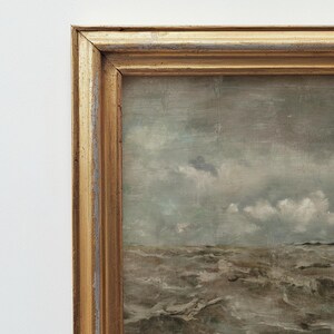 May include: A framed seascape painting with a stormy sea and a cloudy sky. The painting is in a gold frame.