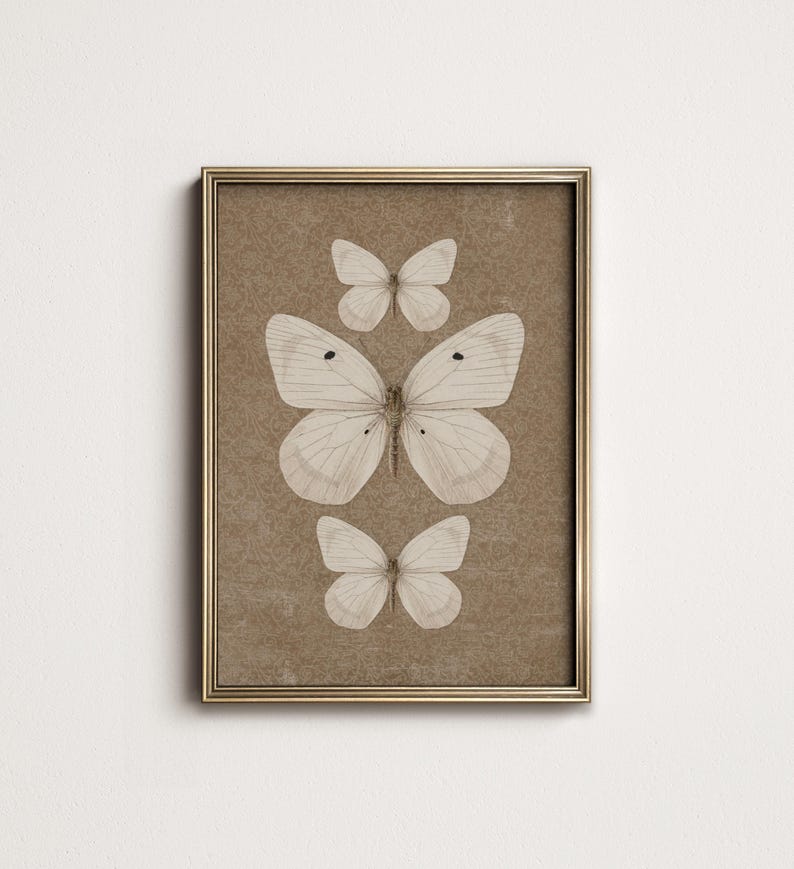May include: A framed print of three white butterflies on a brown background. The butterflies are arranged in a vertical line, with the largest butterfly at the bottom and the smallest butterfly at the top.