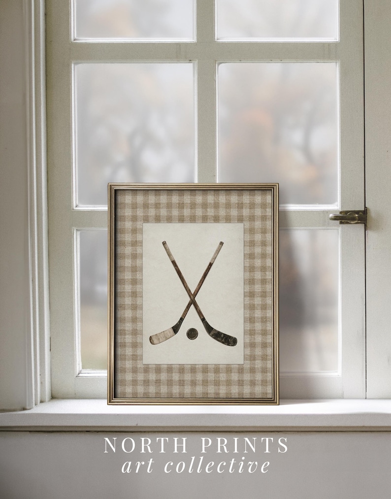 May include: Framed art print featuring crossed hockey sticks and a puck. The artwork is set against a beige and white checkered background, framed in gold. The text "NORTH PRINTS art collective" is at the bottom.