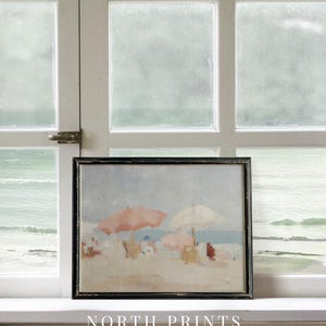 Puede incluir: Pintura enmarcada de una escena de playa con marco negro. La obra representa una playa arenosa con gente, sombrillas y el mar al fondo. La pintura tiene una paleta de colores suaves y apagados con sombrillas rosas y blancas. El texto "NORTH PRINTS art collective" est&aacute; en la parte inferior.