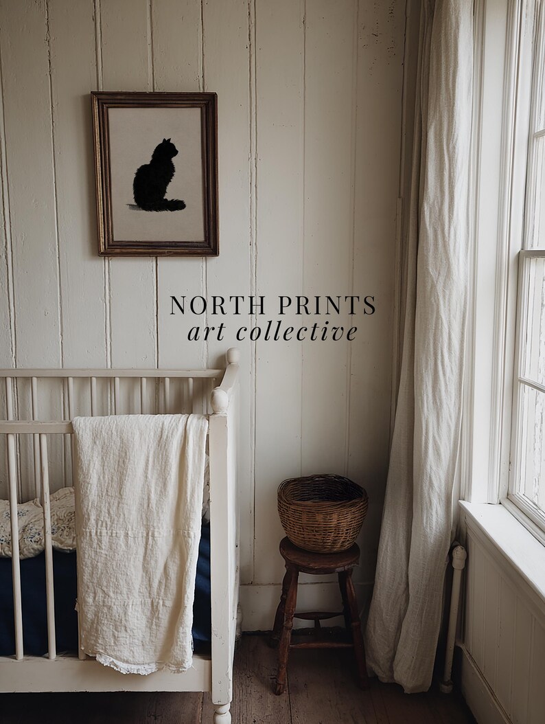 Peut inclure: Une &oelig;uvre encadr&eacute;e repr&eacute;sentant une silhouette de chat noir est accroch&eacute;e au-dessus d'un berceau blanc avec une couverture cr&egrave;me. Un petit tabouret en bois supporte un panier en osier. Le texte "NORTH PRINTS art collective" est visible.