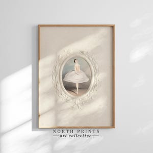 May include: A vintage illustration of a ballerina in a white tutu, framed in a white oval with a decorative floral border. The image is printed on a textured paper and has a light beige background. The frame is made of wood and has a natural finish. The image is titled "NORTH PRINTS - art collective".