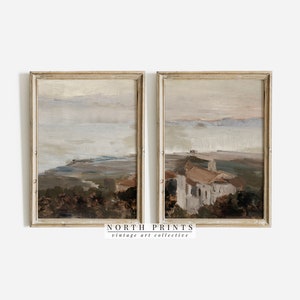 Peut inclure: Deux peintures de paysage encadrées dans un cadre en bois clair. Les peintures sont dans une palette de couleurs douces de bruns, de gris et de bleus. Les peintures représentent un paysage lointain avec un village au premier plan.