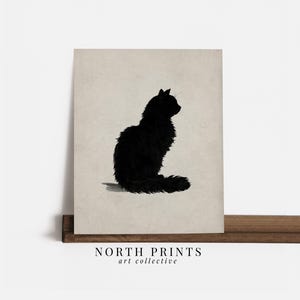 Peut inclure: Impression d'une silhouette de chat noir sur fond beige. Le chat est repr&eacute;sent&eacute; de profil, assis, la queue enroul&eacute;e. L'impression est pr&eacute;sent&eacute;e sur une &eacute;tag&egrave;re en bois. Le texte "NORTH PRINTS art collective" est en bas.