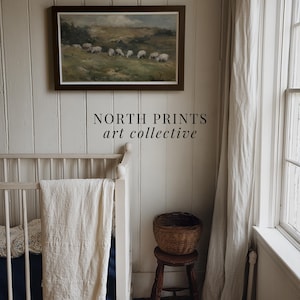 K&ouml;nnte beinhalten: Ein gerahmtes Landschaftsgem&auml;lde mit Schafen auf einer Weide h&auml;ngt &uuml;ber einem wei&szlig;en Kinderbett. Ein kleiner Holzschemel tr&auml;gt einen geflochtenen Korb. Der Text "NORTH PRINTS art collective" steht darunter.