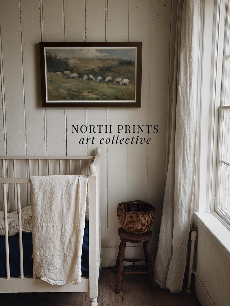 K&ouml;nnte beinhalten: Ein gerahmtes Landschaftsgem&auml;lde mit Schafen auf einer Weide h&auml;ngt &uuml;ber einem wei&szlig;en Kinderbett. Ein kleiner Holzschemel tr&auml;gt einen geflochtenen Korb. Der Text "NORTH PRINTS art collective" steht darunter.