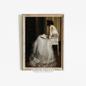 May include: A vintage painting of a woman in a white dress sitting in a chair and reading a book. The painting is framed in a gold frame and has a dark background.
