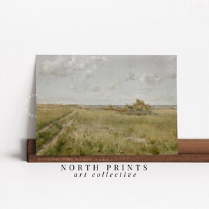 May include: A vintage painting of a dirt road leading to a grassy field with a body of water in the distance. The sky is a light blue with white clouds. The painting is framed and has a white mat.