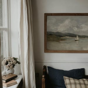 K&ouml;nnte beinhalten: Ein gerahmtes Landschaftsgem&auml;lde eines Segelbootes auf dem Wasser h&auml;ngt &uuml;ber einem Bett mit marineblauen und karierten Kissen. Links vom Bett befindet sich ein Fenster mit wei&szlig;en Vorh&auml;ngen und eine Vase mit Blumen.