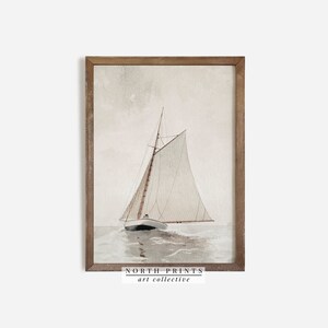 Puede incluir: Una pintura de acuarela de un velero con una vela blanca, navegando en un mar tranquilo. La pintura est&aacute; enmarcada en un marco de madera marr&oacute;n claro. El texto "NORTH PRINTS art collective" est&aacute; impreso debajo de la imagen.