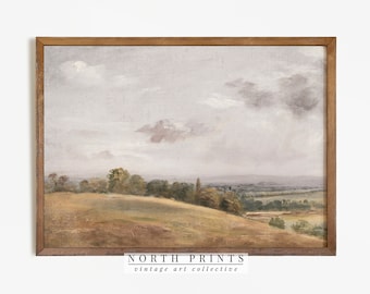 May include: A framed landscape painting depicting a rural scene with a grassy hill, trees, and a distant valley under a cloudy sky. The artwork has a muted colour palette. The wooden frame surrounds the painting. The text "NORTH PRINTS vintage art collective" is at the bottom.