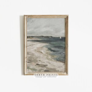 Pu&ograve; includere: Un dipinto incorniciato di un paesaggio marino con una spiaggia sabbiosa, acqua blu e un cielo nuvoloso. Il dipinto &egrave; in una cornice di legno chiaro con una bordura dorata. Il testo "NORTH PRINTS vintage art collective" &egrave; in basso sulla cornice.