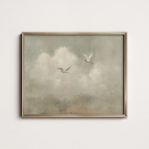 Könnte beinhalten: Ein gerahmtes Kunstwerk mit zwei Möwen, die durch einen bewölkten Himmel fliegen. Das Gemälde in gedämpften Grautönen, Weiß und Beige hat eine Vintage-Ästhetik. Es wird in einem goldfarbenen Rahmen präsentiert. Das Kunstwerk vermittelt ein Gefühl von Frieden und Natur.