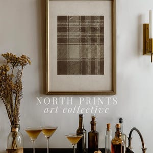May include: A framed print with a brown plaid pattern hangs above a bar cart. The cart holds martini glasses, bottles, and a vase of dried flowers. The text "NORTH PRINTS art collective" is visible.