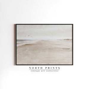 May include: A framed watercolour painting of a beach scene with a light grey sky and a sandy beach with a few birds flying overhead. The painting is framed in a black frame and has the text "NORTH PRINTS vintage art collective" below the image.