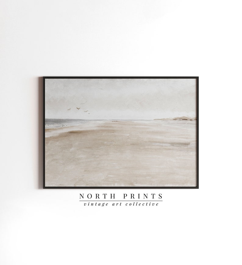 May include: A framed watercolour painting of a beach scene with a light grey sky and a sandy beach with a few birds flying overhead. The painting is framed in a black frame and has the text "NORTH PRINTS vintage art collective" below the image.