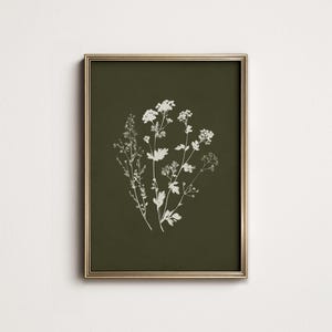 May include: A framed botanical print featuring white floral illustrations on a dark olive green background. The artwork is encased in a gold-colored frame, creating a classic and elegant aesthetic. The print showcases detailed botanical drawings.