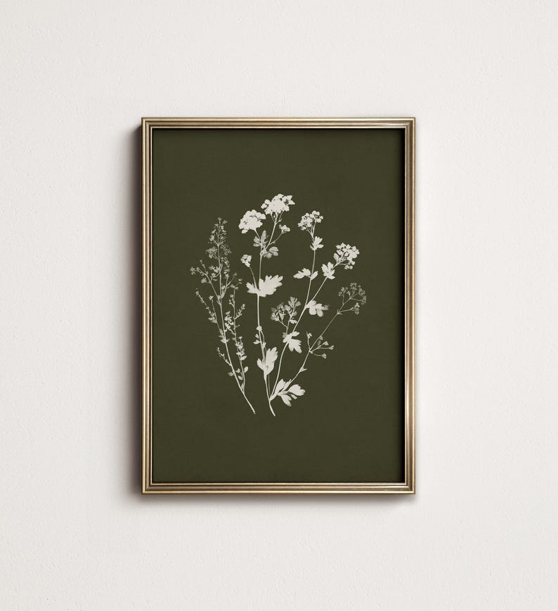 May include: A framed botanical print featuring white floral illustrations on a dark olive green background. The artwork is encased in a gold-colored frame, creating a classic and elegant aesthetic. The print showcases detailed botanical drawings.