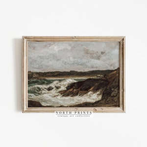 May include: A framed vintage seascape painting depicting a rocky coastline with crashing waves and a cloudy sky. The painting is in a light wood frame and has the text "NORTH PRINTS vintage art collective" at the bottom.