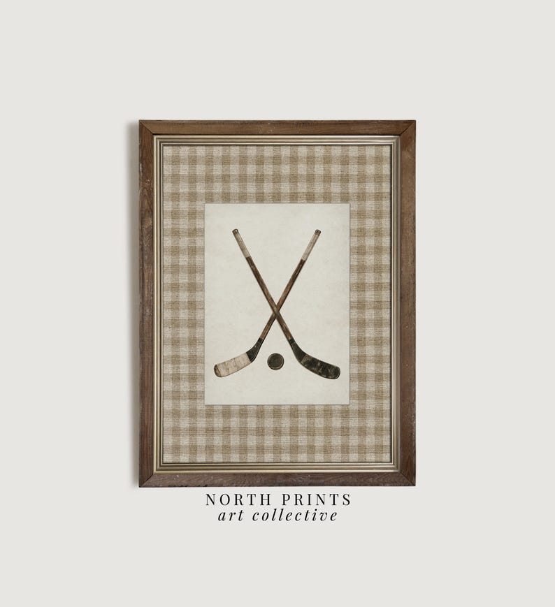 May include: Framed print featuring crossed hockey sticks and a puck. The artwork is set against a cream-colored background with a brown and tan plaid pattern. The frame is a dark brown color. The text "NORTH PRINTS art collective" is at the bottom.
