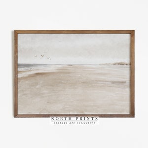 May include: A framed print of a watercolour painting depicting a beach scene with a light brown sandy beach, a light blue ocean, and a cloudy sky. The print is framed in a light brown wood frame. The text "NORTH PRINTS vintage art collective" is printed at the bottom of the print.