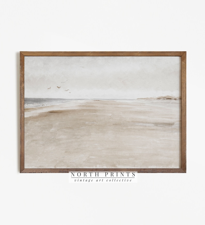 May include: A framed print of a watercolour painting depicting a beach scene with a light brown sandy beach, a light blue ocean, and a cloudy sky. The print is framed in a light brown wood frame. The text "NORTH PRINTS vintage art collective" is printed at the bottom of the print.