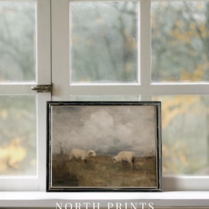 K&ouml;nnte beinhalten: Gerahmtes Kunstwerk mit zwei Schafen, die auf einer Wiese unter einem bew&ouml;lkten Himmel grasen. Das Gem&auml;lde hat eine ged&auml;mpfte Farbpalette mit Braun-, Grau- und Wei&szlig;t&ouml;nen. Das Kunstwerk ist in einem schwarzen Holzrahmen gerahmt. Der Text "NORTH PRINTS art collective" steht unten.