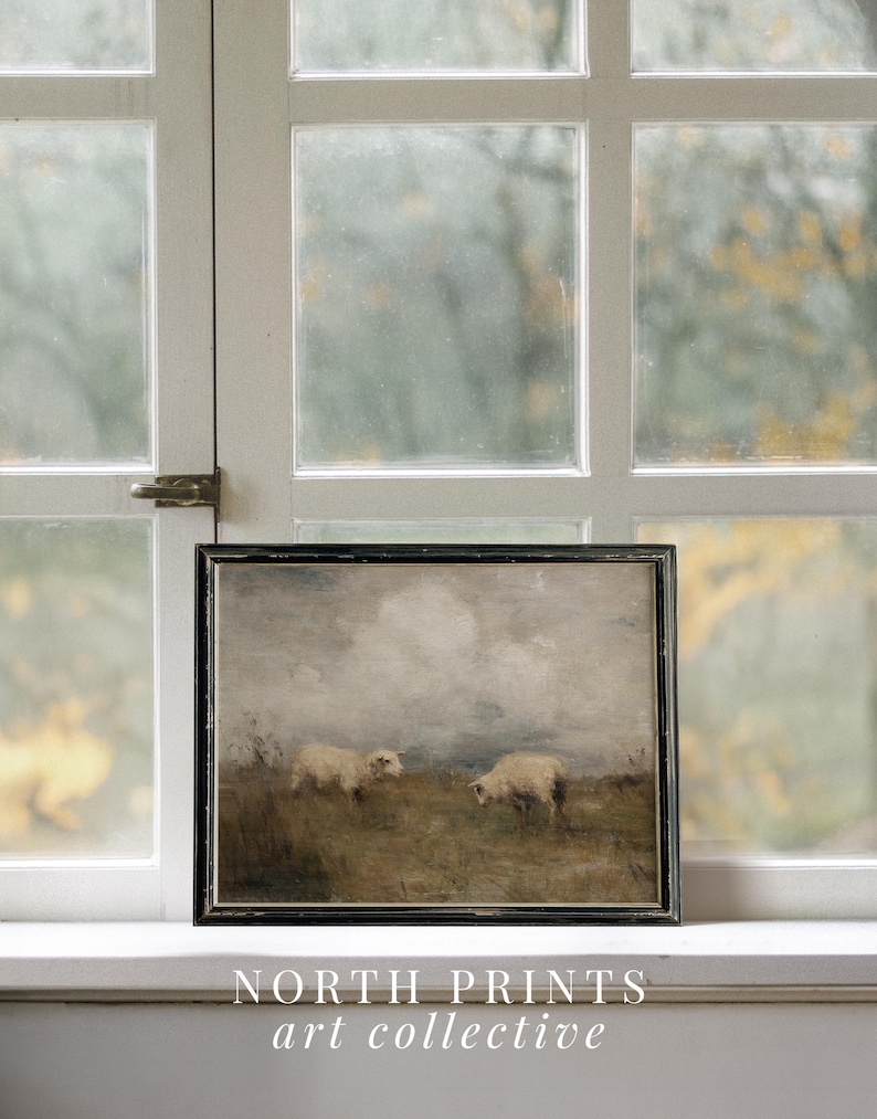 K&ouml;nnte beinhalten: Gerahmtes Kunstwerk mit zwei Schafen, die auf einer Wiese unter einem bew&ouml;lkten Himmel grasen. Das Gem&auml;lde hat eine ged&auml;mpfte Farbpalette mit Braun-, Grau- und Wei&szlig;t&ouml;nen. Das Kunstwerk ist in einem schwarzen Holzrahmen gerahmt. Der Text "NORTH PRINTS art collective" steht unten.