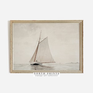 May include: A vintage watercolor painting of a sailboat on the water. The sailboat has a white sail and a brown hull. The water is a light blue color and the sky is a light gray color. The painting is framed in a light wood frame. The text "NORTH PRINTS vintage art collective" is at the bottom of the painting.