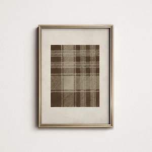 May include: A framed print featuring a brown and beige plaid pattern. The plaid design has a classic, symmetrical arrangement of intersecting lines, creating a textured appearance. The print is set within a gold-colored frame, enhancing its visual appeal.