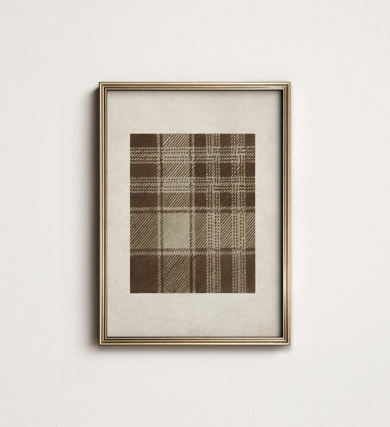 May include: A framed print featuring a brown and beige plaid pattern. The plaid design has a classic, symmetrical arrangement of intersecting lines, creating a textured appearance. The print is set within a gold-colored frame, enhancing its visual appeal.