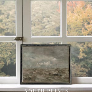 May include: A framed painting of a seascape with a stormy sea and a cloudy sky. The painting is in a black frame and is sitting on a windowsill. The text "NORTH PRINTS art collective" is below the painting.