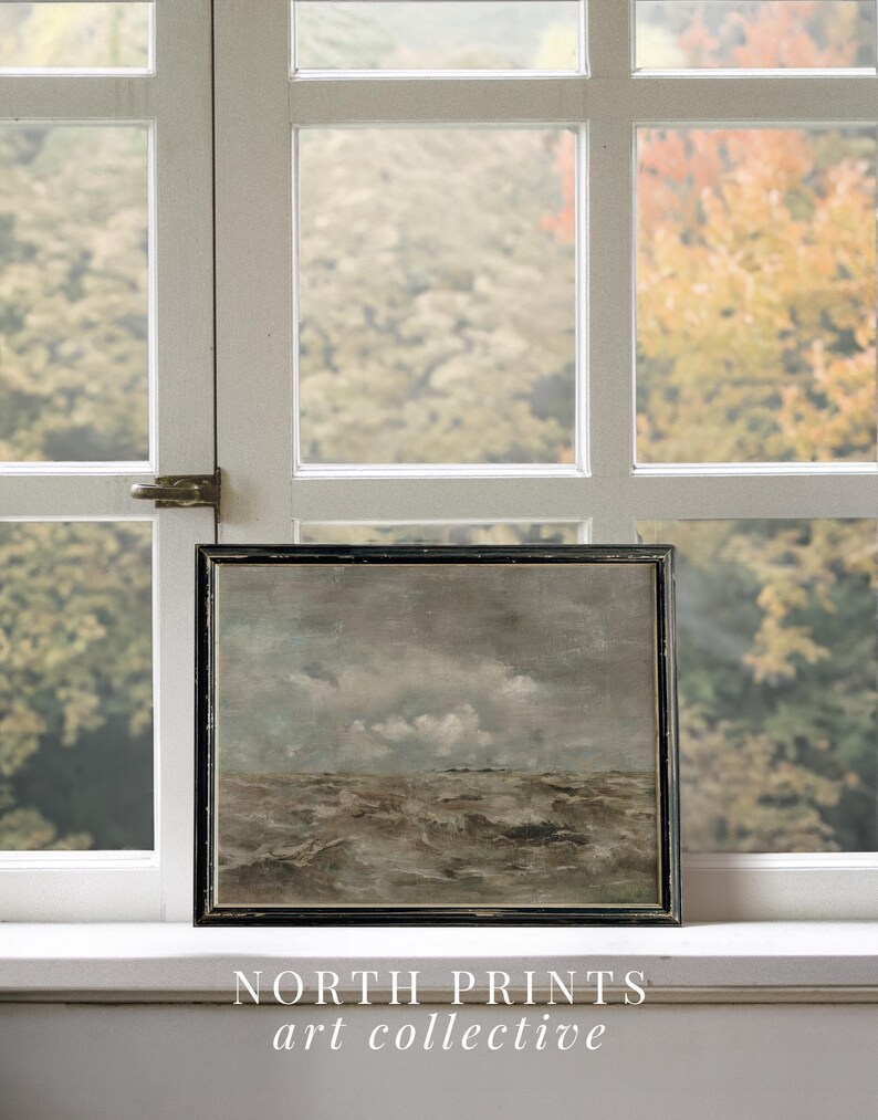 May include: A framed painting of a seascape with a stormy sea and a cloudy sky. The painting is in a black frame and is sitting on a windowsill. The text "NORTH PRINTS art collective" is below the painting.