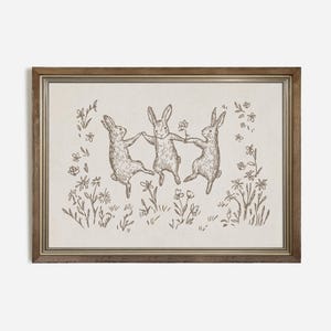 May include: A framed illustration of three rabbits dancing in a field of flowers. The rabbits are drawn in a simple, whimsical style, and the flowers are delicate and colorful.