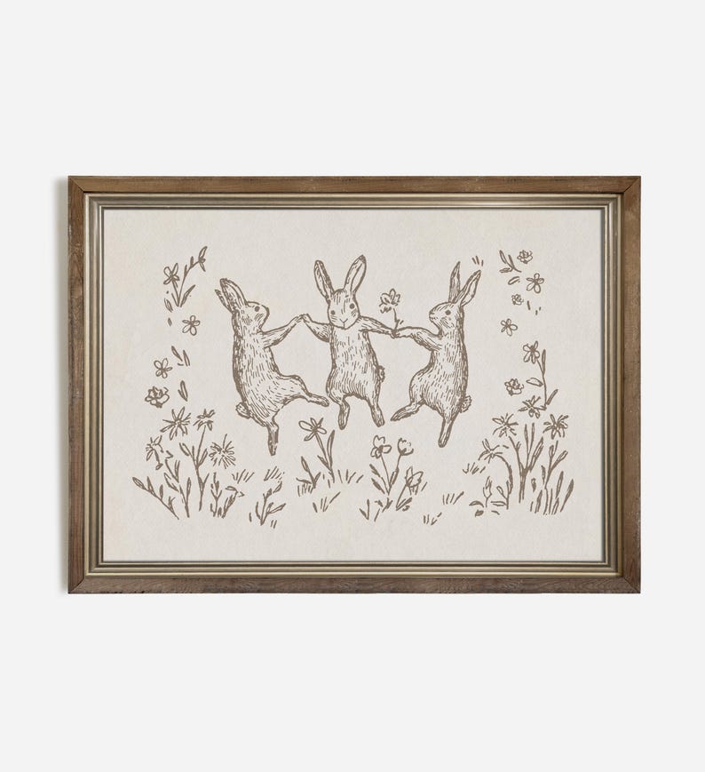 May include: A framed illustration of three rabbits dancing in a field of flowers. The rabbits are drawn in a simple, whimsical style, and the flowers are delicate and colorful.