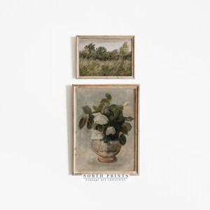 Op de afbeelding: Twee ingelijste vintage schilderijen. Het bovenste schilderij is een landschapssc&egrave;ne met een veld met groen gras en bomen op de achtergrond. Het onderste schilderij is een stilleven van witte bloemen in een vaas.
