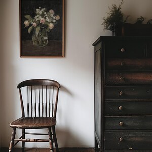 May include: A vintage wooden chair with a dark brown finish sits in front of a dark wood dresser with six drawers. A framed painting of a vase of flowers hangs on the wall behind the chair. The text "NORTH PRINTS art collective" is printed on the floor in front of the chair.