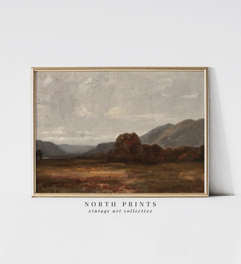 May include: A vintage landscape painting in a brown wooden frame. The painting depicts a rolling hillside with a forest in the foreground and a mountain range in the background. The sky is a light blue with white clouds.