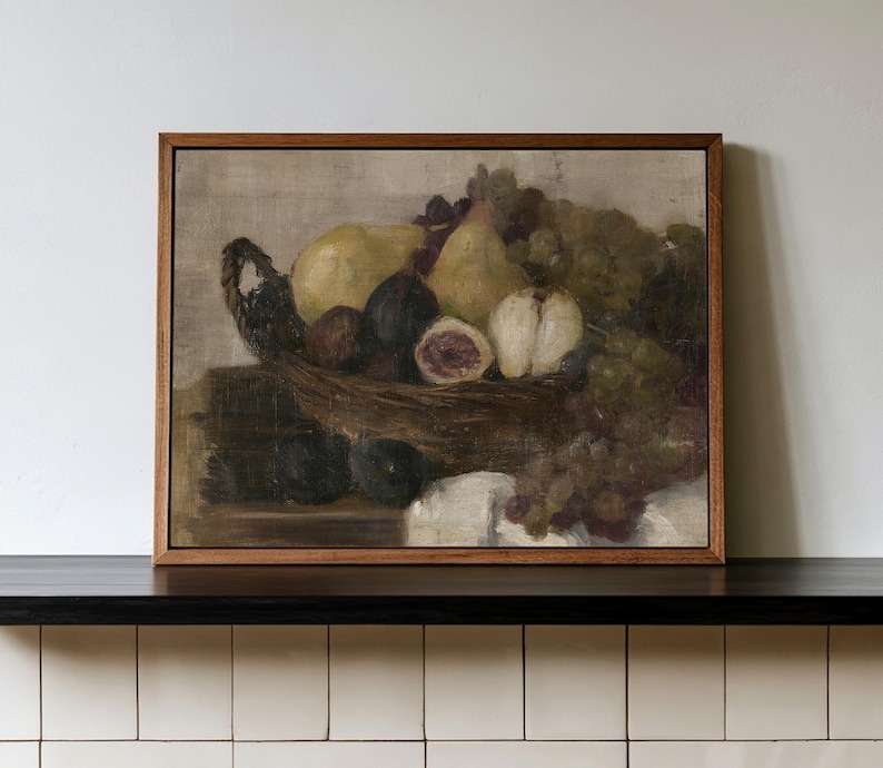 K&ouml;nnte beinhalten: Ein gerahmtes &Ouml;lgem&auml;lde, das ein Stillleben mit Obst in einem geflochtenen Korb zeigt. Die Komposition umfasst gelbe Birnen, dunkelviolette Feigen und gr&uuml;ne Weintrauben auf einer Fl&auml;che mit einem wei&szlig;en Tuch, gehalten in gedeckten, erdigen Farbt&ouml;nen.