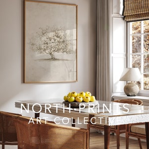 Op de afbeelding: Een ingelijste print van een boom met een lichtbruine achtergrond. De print hangt aan een muur in een eetkamer met een houten tafel en stoelen. Op de tafel staat een kom met gele appels. De tekst "NORTH PRINTS ART COLLECTI" is zichtbaar op de tafel.