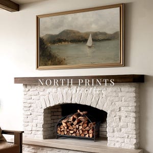 May include: A framed landscape painting with a sailboat on the water hangs above a white brick fireplace. The painting has a gold frame and depicts a serene coastal scene. The fireplace has a dark wood mantel and a black metal log holder.